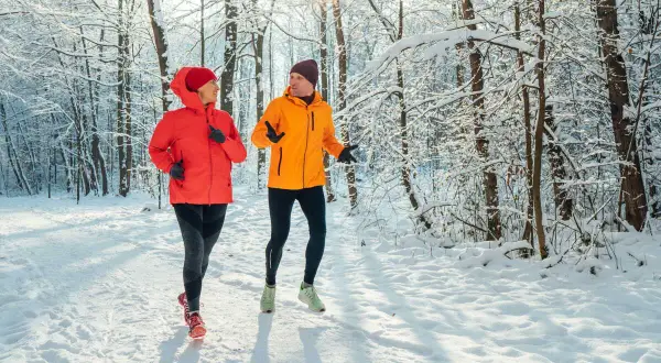 Un couple profite de l'air frais en courant sous la neige dans une forêt enneigée.