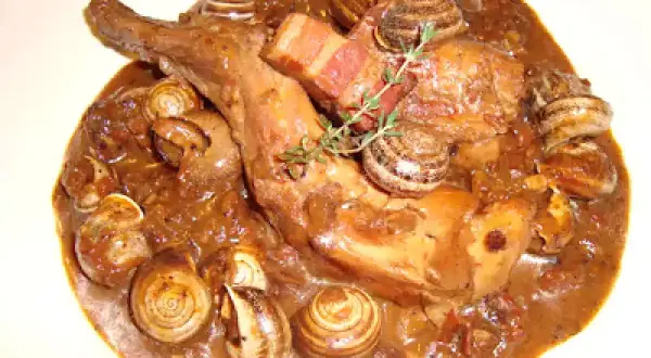 Guiso de conejo con caracoles, bañado en una rica salsa oscura, con trozos de tocino y una ramita de romero.
