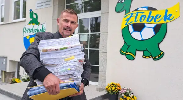 Mężczyzna z dużą stertą dokumentów przed żłobkiem z logo żółwia.