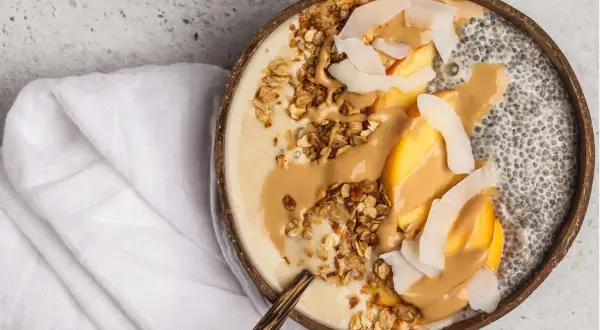 Cremige Chia Overnight Oats im Kokosnussschalen-Bowl mit Pfirsich, Granola und Erdnussbutter. Ein gesunder Start in den Tag!