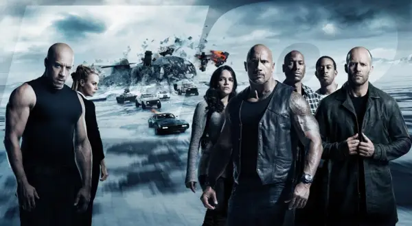 Die Hauptdarsteller der besetzung von Fast & Furious 8 stehen vor einer eisigen Landschaft mit explodierenden Fahrzeugen und einem Helikopter.