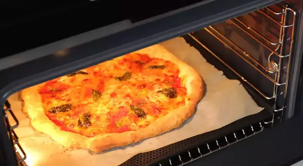 Une pizza maison dorée et appétissante est en pleine cuisson dans un four moderne. Le fromage fond et les herbes parfument l'air.