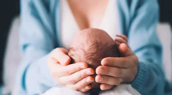 Delikatne dłonie otulają główkę noworodka, ukazując troskę i miłość. Szybko zarastające ciemiączko to naturalny proces, a ten obraz to dowód na to, jak szybko dzieci rosną.