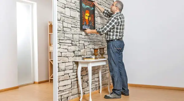 Mann hängt Bild an Trockenbauwand. Ein Mann baut eine Trockenbauwand und dekoriert sie mit einem Bild.