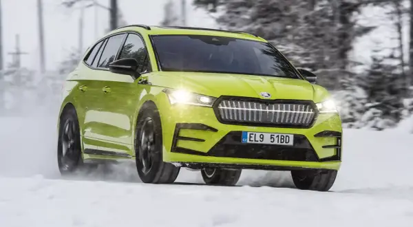 En ljusgrön Skoda Enyaq testas i snö. Bilen kör genom ett vinterlandskap med träd i bakgrunden.
