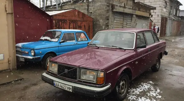 En vinröd Volvo 244 DLS står parkerad bredvid en blå bil i snöfall.
