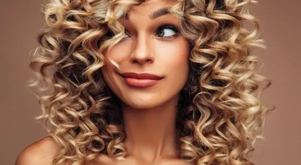 Kobieta z burzą blond loków, loki krótkie kręcone włosy tworzą ramę dla jej twarzy.
