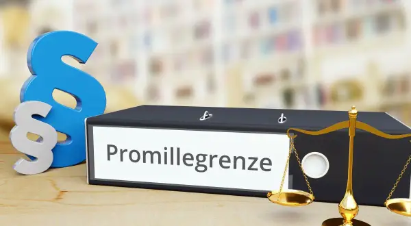 Ein Ordner mit der Aufschrift "Promillegrenze" steht neben Paragraphen-Symbolen und einer Waage. Dies symbolisiert die rechtlichen Aspekte der Promillegrenze im Straßenverkehr.