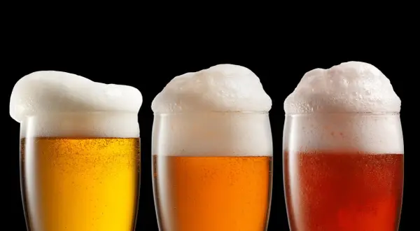 Tre bicchieri di birra con abbondante schiuma, uno biondo, uno ambrato e uno rosso.