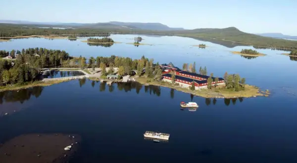 Vacker vy över en sjö med röda byggnader och båtar vid **kraja Arjeplog**.