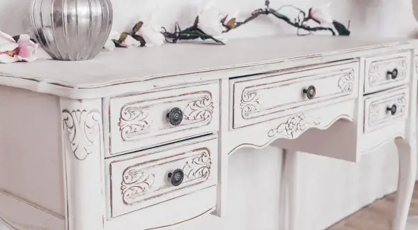 Un mobile da marrone a bianco, con dettagli intagliati e pomelli antichi. Un vaso d'argento e fiori decorano il piano.