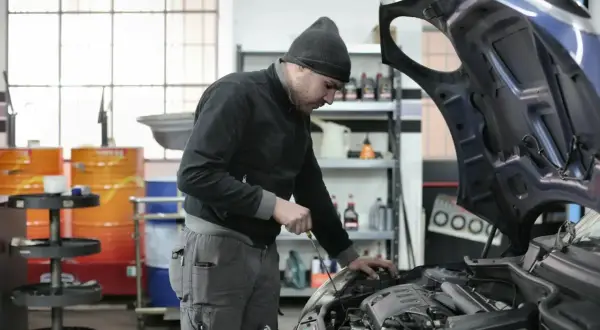 Mechanik sprawdza silnik, zastanawiając się, ile kosztuje roboczogodzina w warsztacie samochodowym.