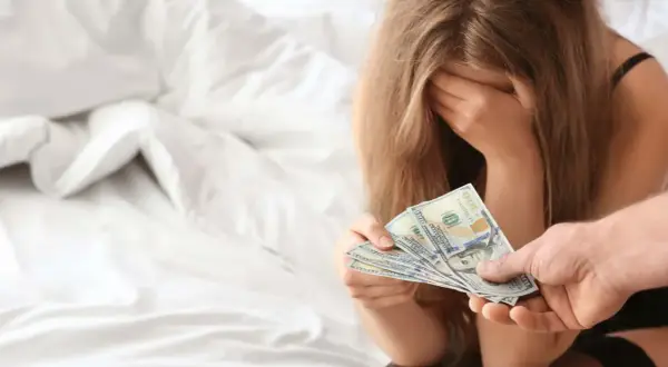 Kobieta z ręką na twarzy otrzymuje pieniądze. To obrazuje problem sutenerstwa i tego, co to znaczy.