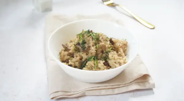 Miseczka kremowego risotto z grzybami, posypana ziołami, na jasnym obrusie.