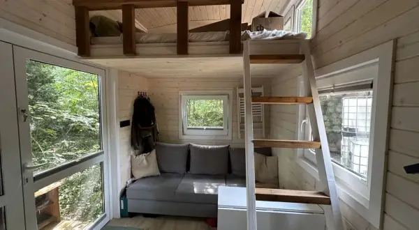 Clevere tiny house bett ideen: ein gemütliches Hochbett über einer Couch, mit Leiter und Fensterblick ins Grüne.