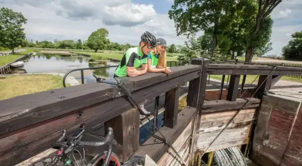Para rowerzystów odpoczywa przy śluzie, podziwiając malownicze **trasy rowerowe Augustów**.