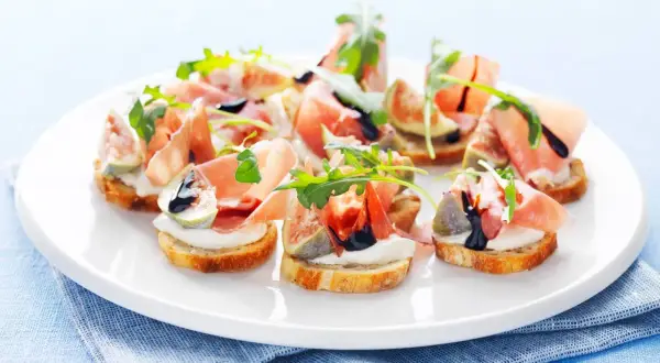En tallrik med läckra crostini med lufttorkad skinka, färska fikon, krämig ost och ruccola, ringlad med balsamvinäger.
