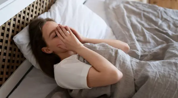 Vrouw in bed, handen voor gezicht, kan niet slapen door onrust in hoofd.