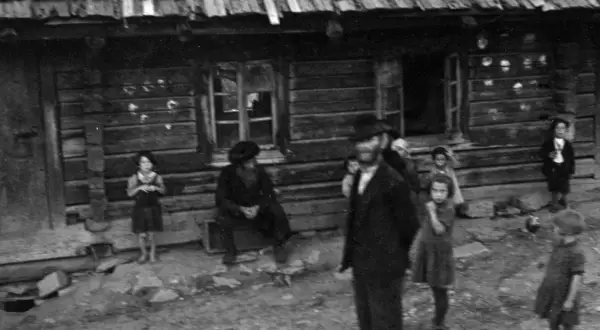 Kinder und Erwachsene stehen vor einem Holzhaus. Die Szene erinnert an die **Judenverfolgung** und die damit verbundene Not.