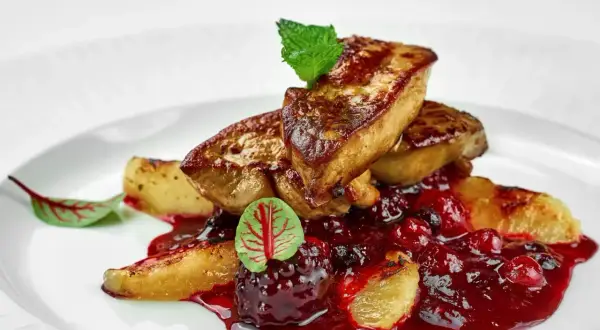 Tranches de foie gras poêlé, nappées d'une sauce aux fruits rouges, garnies d'une feuille de menthe et d'une petite feuille rouge. L'épice foie gras est sublimée par cette présentation.
