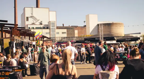 Menschen genießen das Street Food Festival Bergisch Gladbach mit vielen Essensständen und bunter Atmosphäre vor Industriebauten.