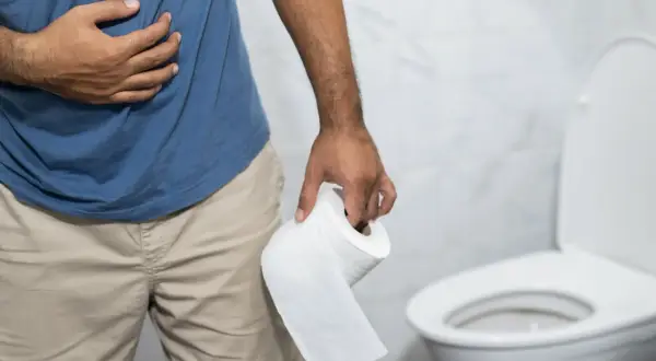 Mężczyzna trzymający papier toaletowy, z ręką na brzuchu, w łazience. Wygląda na to, że ma **biegunkę po alkoholu**.