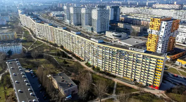 Długi, falisty budynek mieszkalny, znany jako falowiec gdańsk, otoczony zielenią i innymi blokami.