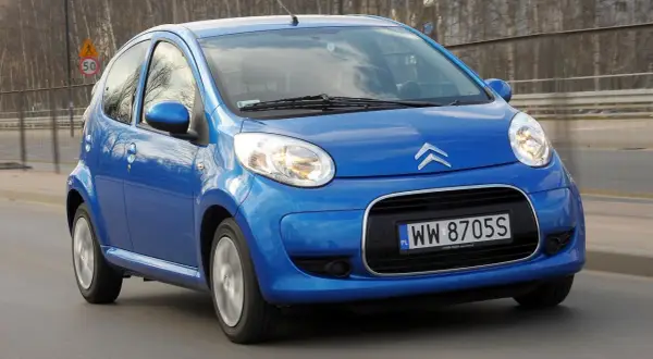 Niebieski Citroen C1 pędzi po drodze, odbijając światła miasta w swoich błyszczących reflektorach.