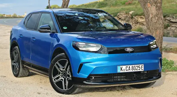 Niebieski Ford Capri 2025, nowoczesny elektryczny SUV, zaparkowany na żwirowej drodze obok drzewa.