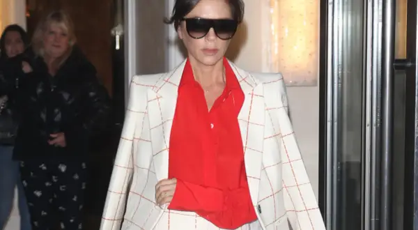 Victoria Beckham, con un traje de cuadros blanco y naranja y camisa roja, sale de un edificio.