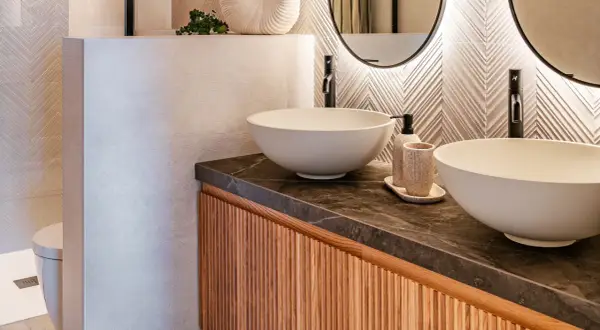 Modernos cuartos de baños con lavabos sobre encimera, grifería negra y detalles en madera.