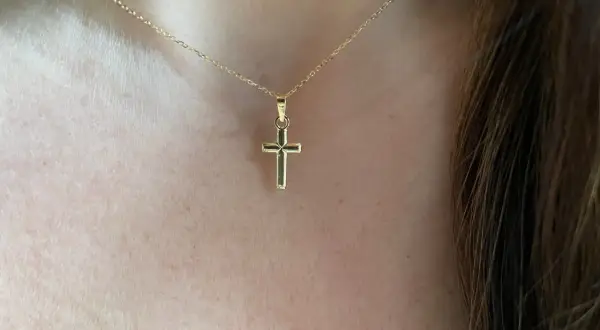 Una delicada cadena de oro sostiene una cruz de oro pequeña, un símbolo de fe y elegancia.