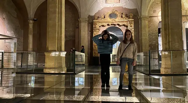 Due ragazze esplorano il Palazzo Madama, con un pavimento in vetro che rivela antiche rovine sottostanti.