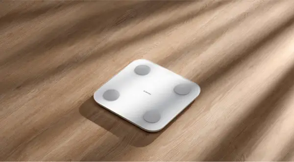 Biała waga Xiaomi na drewnianym blacie. To urządzenie mierzy masę ciała, pomagając zrozumieć, co to masa w elektryce.