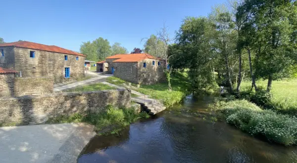 Casas de piedra con tejados rojos y ventanas azules junto a un río. Un lugar idílico que ver en Vila de Cruces.