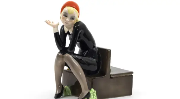 Figura in ceramica di donna con cappello rosso e abito nero, seduta su una panca. Un esempio per capire come riconoscere le bambole Lenci.