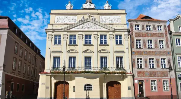 Pałac Działyńskich w Poznaniu, z bogatymi zdobieniami i orłem na szczycie, dumnie prezentuje się na tle błękitnego nieba.
