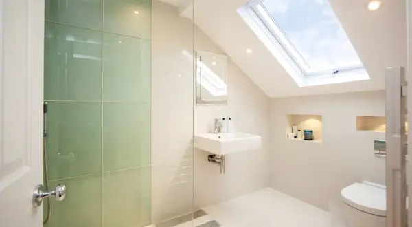 Moderno baño con ducha de cristal verde, lavabo flotante y tragaluz. Ideas para como decorar un baño con estilo y luz natural.
