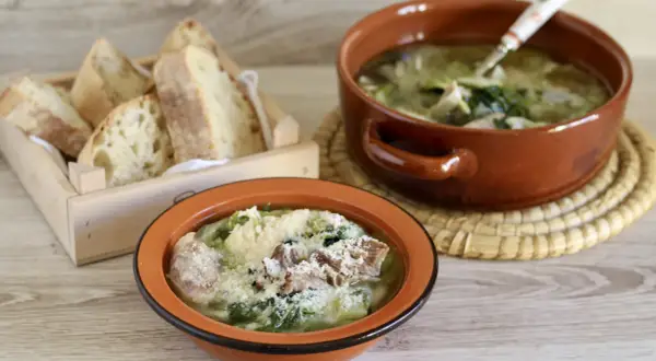 Two bowls of hearty Italian soup with greens and meat, served with crusty bread in a wooden crate.