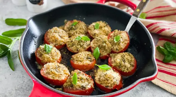 Pomodori gratinati in padella, ripieni di pangrattato e erbe aromatiche, guarniti con basilico fresco.