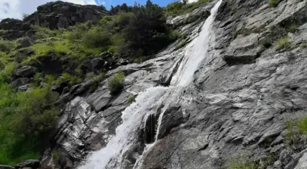 Una hermosa cascada en Madrid, cayendo por rocas grises y vegetación verde bajo un cielo azul con nubes blancas.