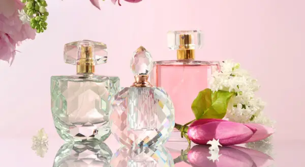 Trzy flakoniki perfum i kwiaty na różowym tle.
