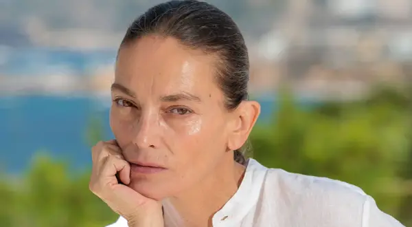 Retrato de **Laura Ponte joven**, con la mano apoyada en la barbilla, mirando pensativa. Fondo desenfocado de mar y vegetación.