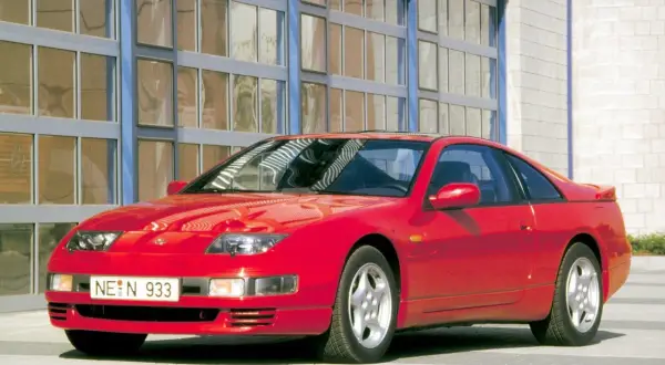 Czerwony Nissan 300zx z lat 90. stoi przed budynkiem z dużymi, przeszklonymi drzwiami.