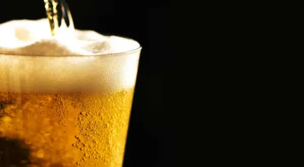 Birra ghiacciata che cola in un bicchiere, creando una schiuma densa e invitante. Le bollicine danzano nel liquido dorato.