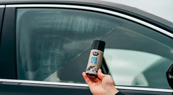 Dłoń trzyma puszkę preparatu K2 FOX ANTI-FOG, który zapobiega parowaniu szyb w samochodzie.