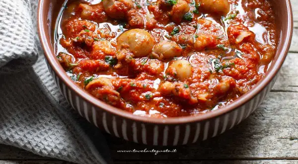 Seppie in padella, succulente e profumate, servite in una ciotola marrone con un contorno di tovagliolo grigio.