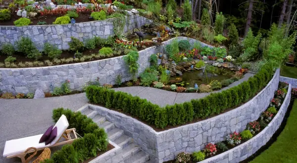 Giardino terrazzato con laghetto e cascata. Muri in pietra che creano livelli, illustrando la differenza tra muro di sostegno e muro di contenimento.