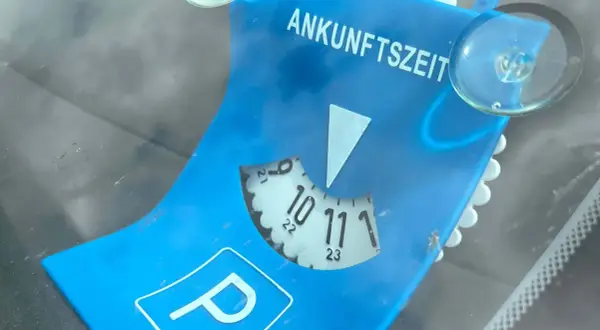 Blaue Parkscheibe mit der Aufschrift "ANKUNFTSZEIT". Die Scheibe ist auf 10:30 Uhr eingestellt, was 15 Minuten Parkzeit bedeutet.