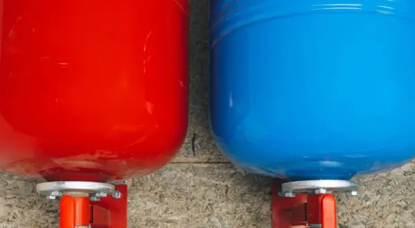 Deux réservoirs, un rouge et un bleu, sont fixés à un mur. Ce sont des éléments essentiels d'un système de chauffage, fonctionnant comme un vase d'expansion.